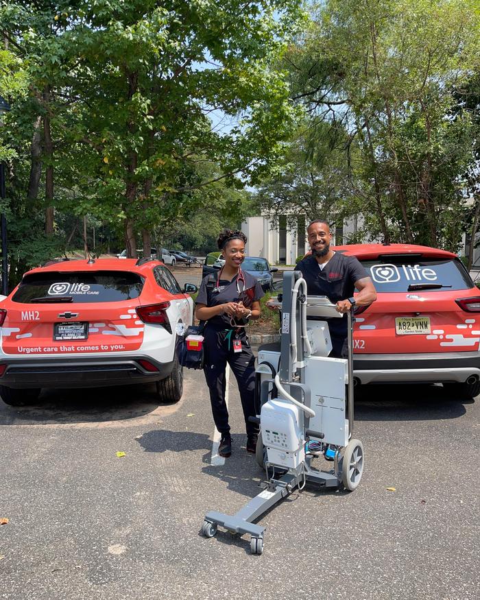 Two Life Primary Care clinicians outside with a portable x-ray unit and two marked practice cars